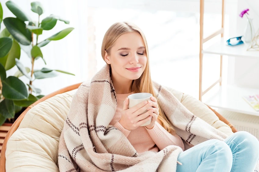 Zufriedene Frau mit Kaffeetasse in der Hand auf einem Sessel nach erfolgreicher Bruststraffung